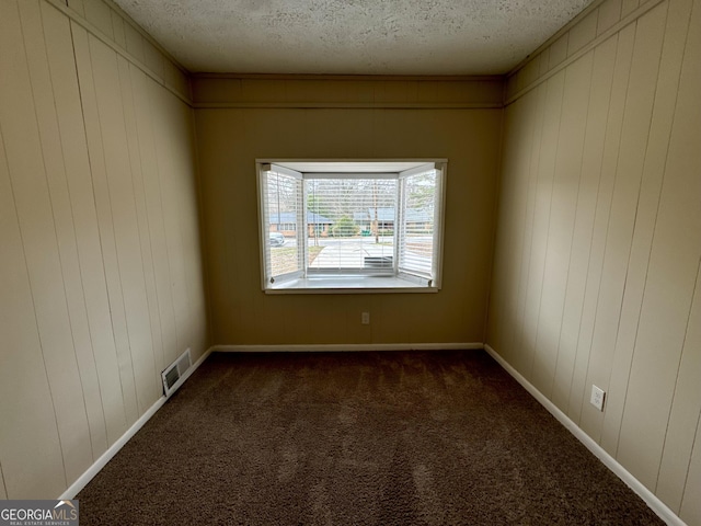 empty room featuring visible vents, dark carpet, a textured ceiling, and baseboards