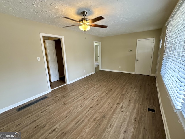 empty room with a ceiling fan, wood finished floors, visible vents, and baseboards