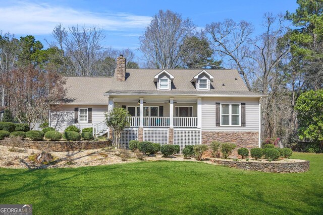 cape cod house featuring a front yard, covered porch, stone siding, and a chimney