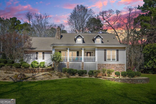 view of front of home with a chimney, stone siding, covered porch, and a front yard