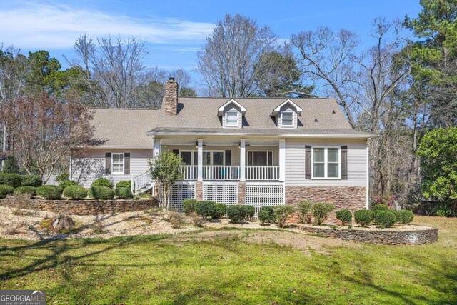 cape cod home featuring stone siding, a porch, a chimney, and a front yard