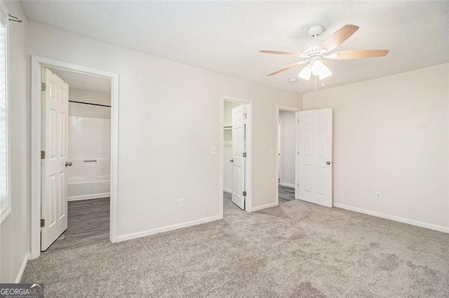 unfurnished bedroom featuring a walk in closet, baseboards, carpet floors, and a textured ceiling