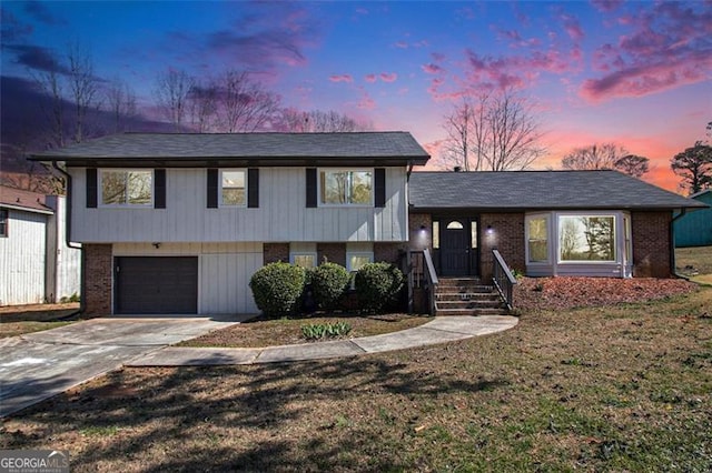 split level home with a front lawn, an attached garage, brick siding, and driveway