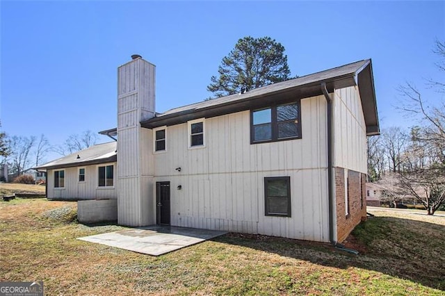 rear view of house featuring a patio, a lawn, and a chimney