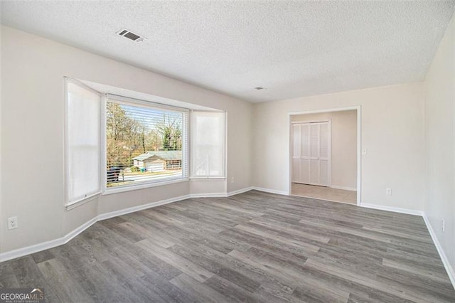 empty room with visible vents, baseboards, a textured ceiling, and wood finished floors