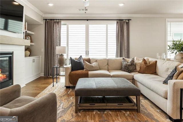 living area featuring visible vents, ornamental molding, recessed lighting, wood finished floors, and a glass covered fireplace