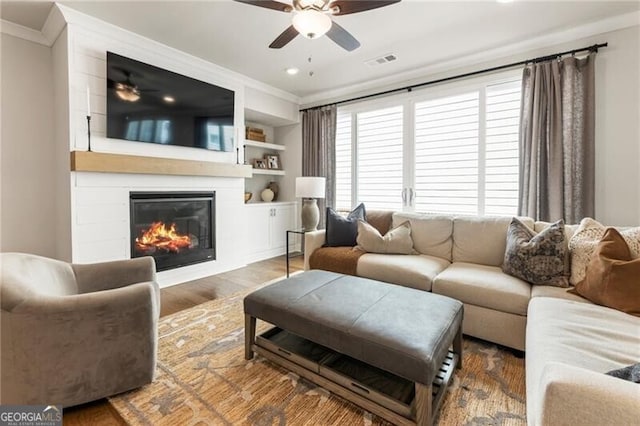 living area with visible vents, ornamental molding, wood finished floors, a large fireplace, and ceiling fan