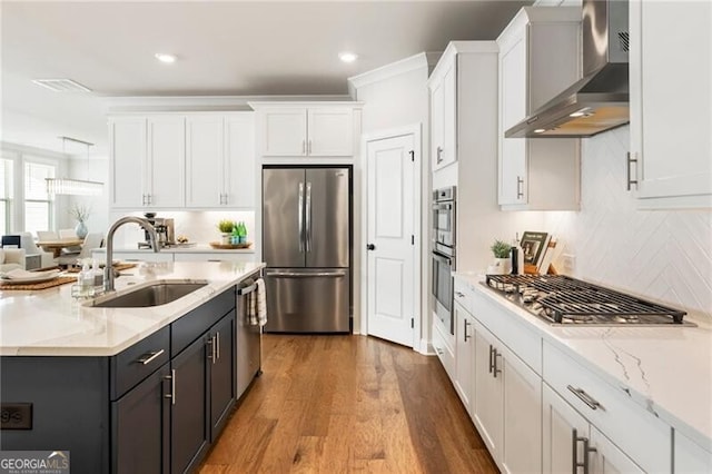 kitchen with wall chimney range hood, decorative backsplash, white cabinets, stainless steel appliances, and a sink