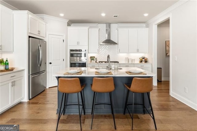 kitchen with wall chimney range hood, a breakfast bar, appliances with stainless steel finishes, white cabinets, and a sink