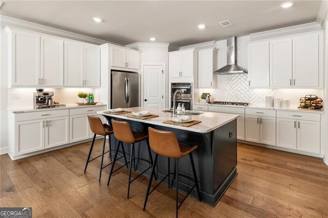 kitchen featuring stainless steel appliances, wood finished floors, a breakfast bar area, and wall chimney exhaust hood