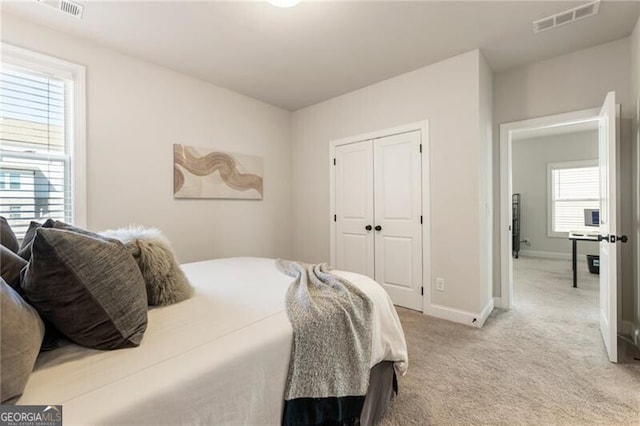 bedroom with visible vents, baseboards, light colored carpet, and a closet