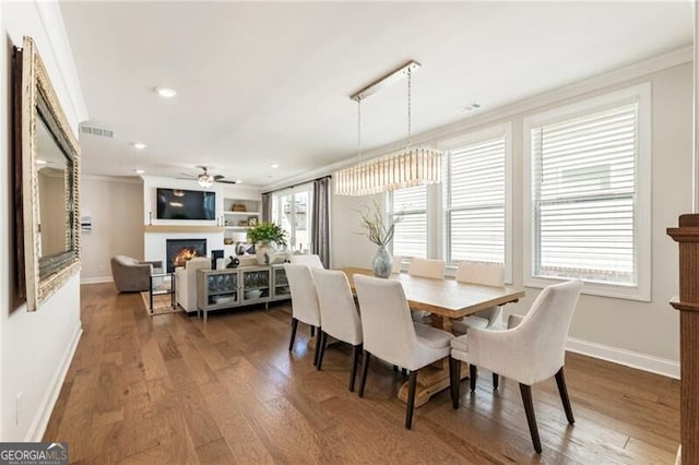 dining room with wood finished floors, visible vents, a warm lit fireplace, and baseboards