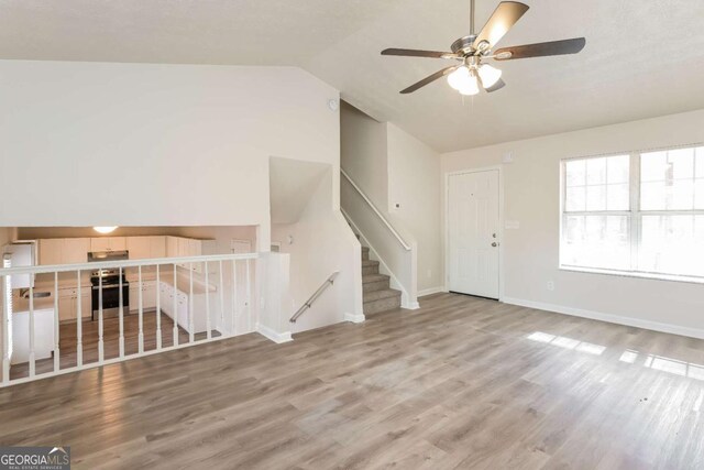 unfurnished living room with ceiling fan, baseboards, wood finished floors, and vaulted ceiling