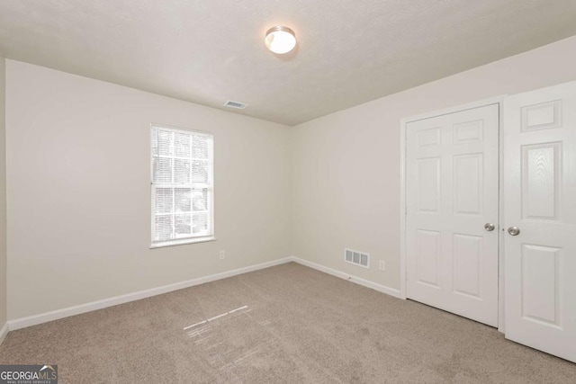 unfurnished bedroom featuring visible vents, baseboards, light colored carpet, and a textured ceiling