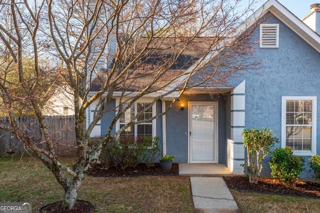 view of front facade featuring stucco siding, a front lawn, and fence