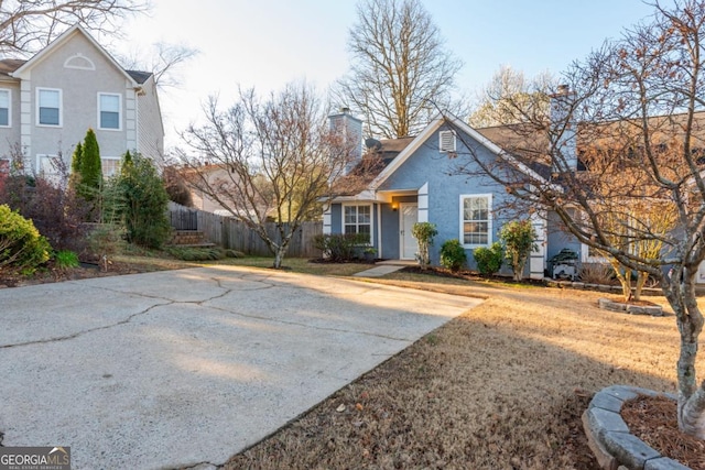 view of front of property with stucco siding, driveway, a chimney, and fence