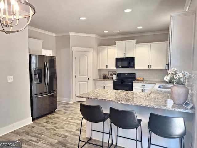 kitchen with black appliances, white cabinets, a peninsula, and tasteful backsplash