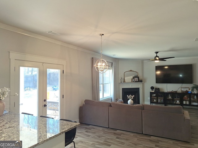 living room with visible vents, crown molding, ceiling fan with notable chandelier, french doors, and wood finished floors