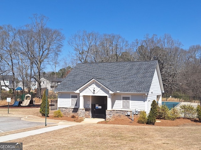 view of front of home with stone siding, a shingled roof, a playground, and fence