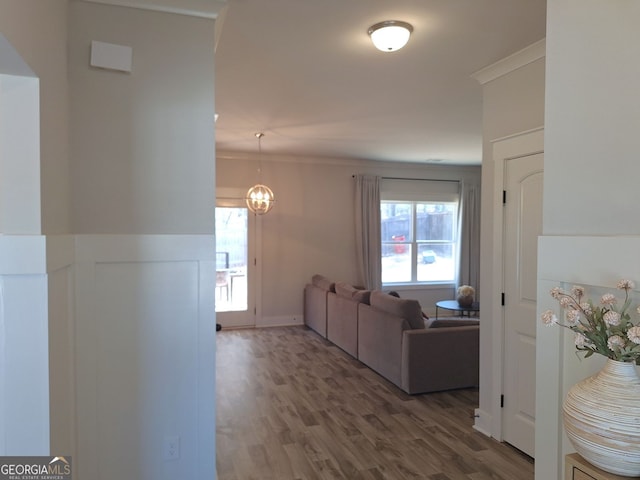 hallway featuring a notable chandelier, wood finished floors, and ornamental molding