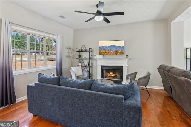 living room featuring visible vents, a warm lit fireplace, baseboards, and wood finished floors