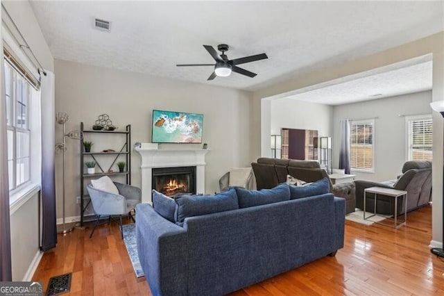 living area featuring visible vents, ceiling fan, baseboards, a lit fireplace, and wood finished floors