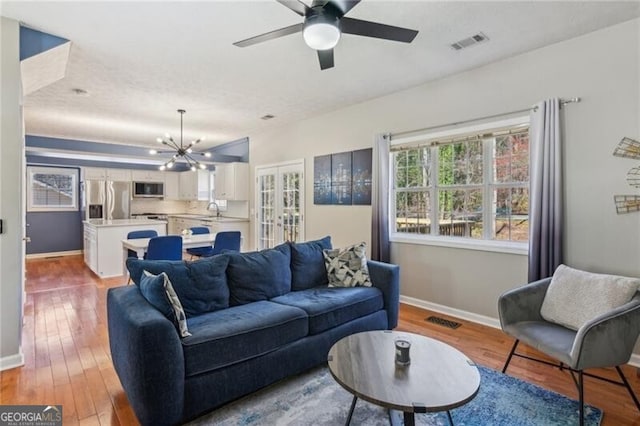 living area with ceiling fan with notable chandelier, baseboards, visible vents, and wood-type flooring