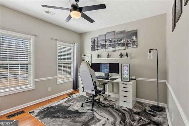 office space featuring a ceiling fan, wood finished floors, visible vents, and baseboards