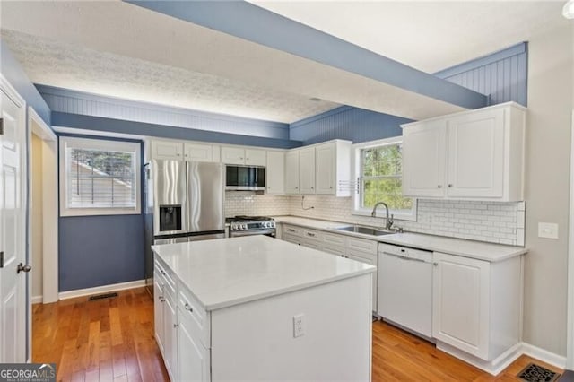 kitchen with a center island, stainless steel appliances, light wood-style floors, white cabinetry, and a sink