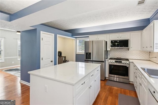 kitchen with stainless steel appliances, backsplash, dark wood-style flooring, and white cabinetry