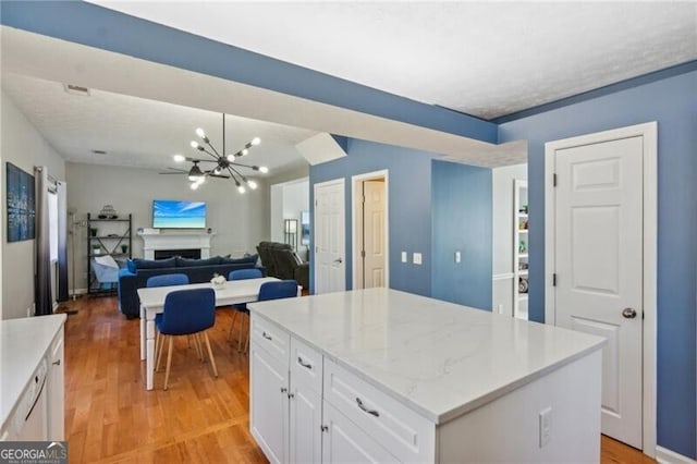 kitchen featuring light wood finished floors, visible vents, a fireplace, a notable chandelier, and white cabinets