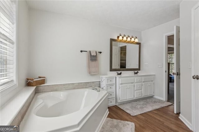 full bathroom with baseboards, a garden tub, double vanity, wood finished floors, and a sink