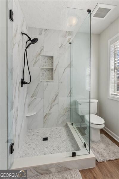 bathroom featuring a marble finish shower, visible vents, toilet, and wood finished floors