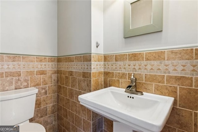 half bathroom with wainscoting, toilet, and a sink