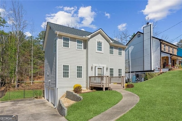 rear view of property featuring a lawn, a deck, fence, concrete driveway, and an attached garage