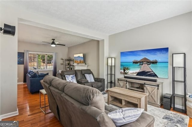 living area with ceiling fan, a textured ceiling, baseboards, and wood finished floors