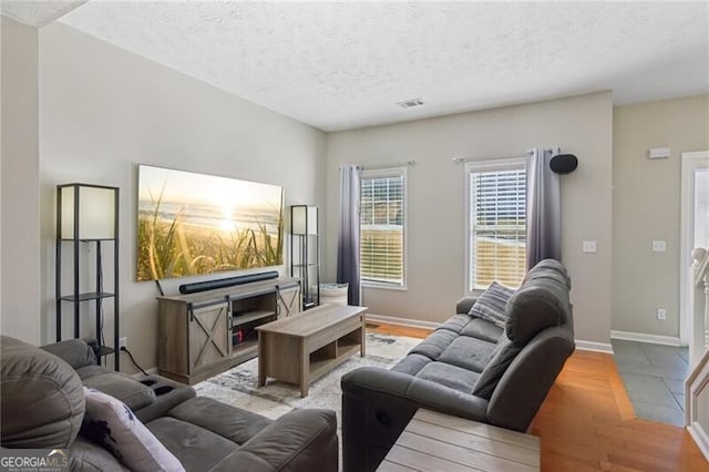 living room featuring visible vents, baseboards, a textured ceiling, and wood finished floors