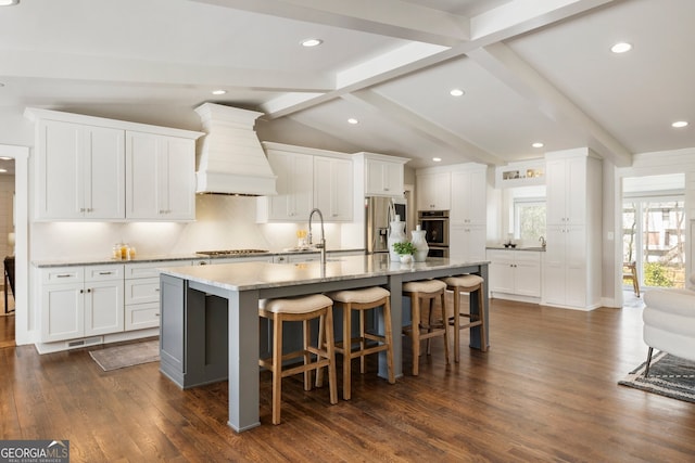 kitchen featuring a kitchen bar, lofted ceiling with beams, custom range hood, stainless steel appliances, and a sink