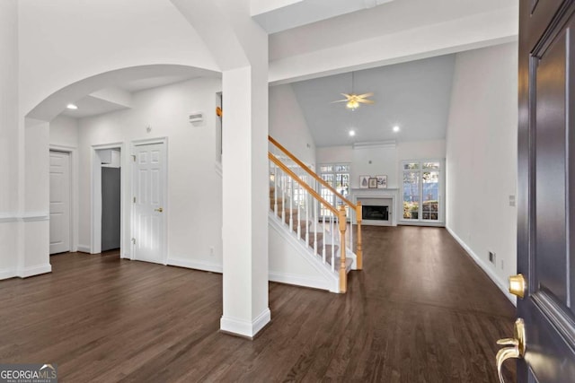 entryway with a fireplace, dark wood-style floors, arched walkways, and baseboards