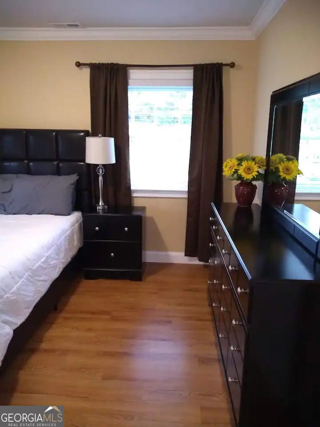 bedroom featuring visible vents, ornamental molding, baseboards, and wood finished floors