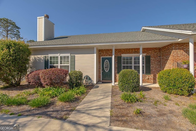 view of exterior entry featuring brick siding, a chimney, and roof with shingles