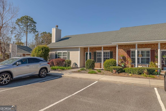 view of front of property with brick siding, uncovered parking, a chimney, and roof with shingles