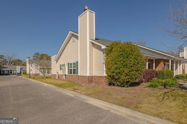 view of side of property with a lawn, brick siding, and a chimney