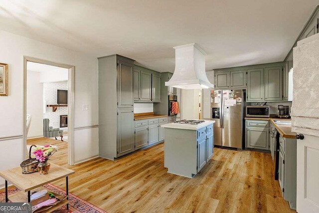 kitchen with light wood-style floors, premium range hood, appliances with stainless steel finishes, and a center island