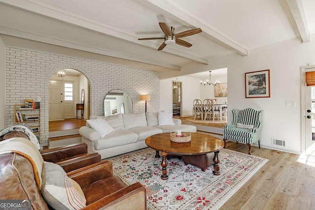 living area with visible vents, beamed ceiling, ceiling fan with notable chandelier, wood finished floors, and arched walkways