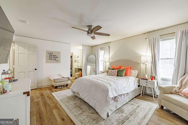 bedroom with light wood finished floors, ensuite bathroom, and a ceiling fan