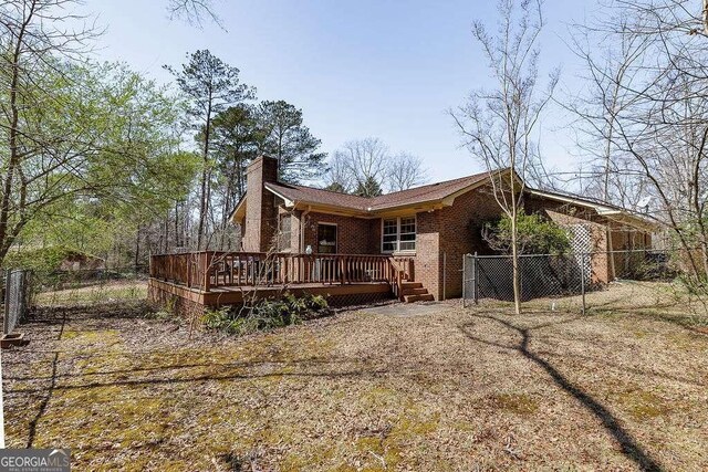 rear view of property with brick siding, a deck, a chimney, and fence