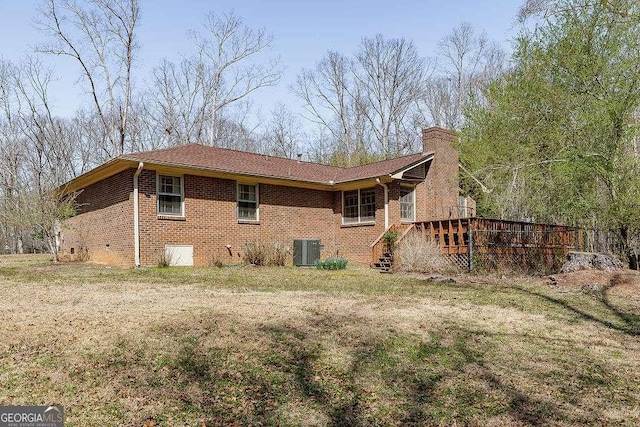 view of side of property featuring brick siding, a wooden deck, a lawn, cooling unit, and a chimney