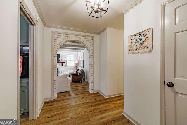 corridor with baseboards, ornamental molding, light wood-style flooring, arched walkways, and a notable chandelier