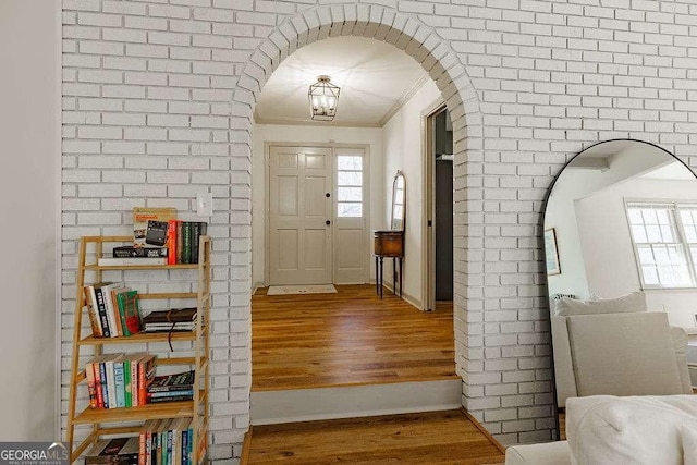 entrance foyer featuring brick wall, crown molding, baseboards, wood finished floors, and arched walkways